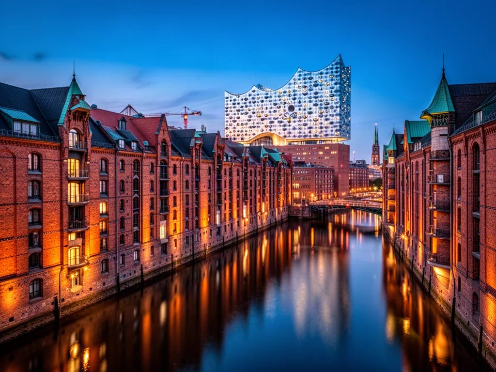 Widok na oświetloną dzielnicę spichlerzy Speicherstadt oraz nowoczesną filharmonię Elbphilharmonie w Hamburgu o zmierzchu.